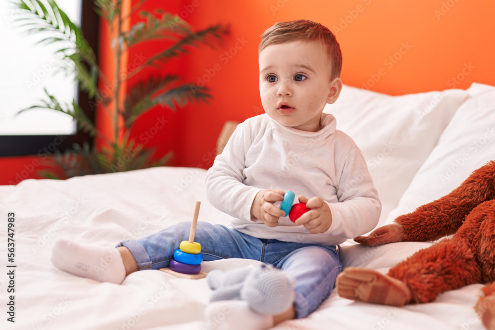 Naklejka premium Adorable caucasian baby playing with toys sitting on bed at bedroom