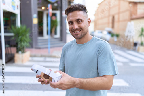 Young hispanic man smiling confident holding headphones at street