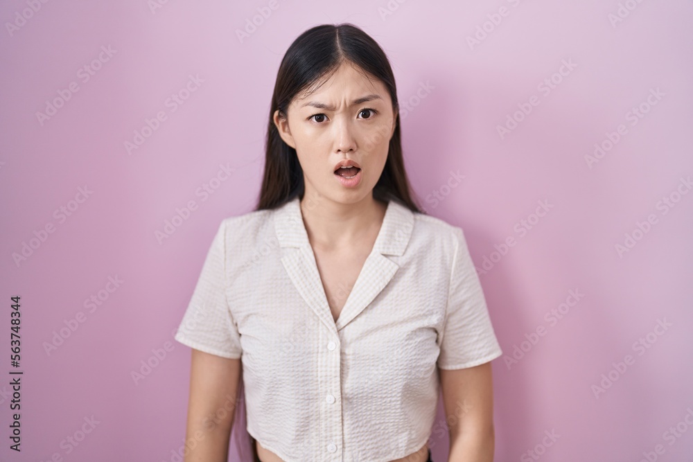 Chinese young woman standing over pink background in shock face, looking skeptical and sarcastic, surprised with open mouth Chinese young woman standing over pink background in shock face, looking skeptical and sarcastic, surprised with open mouth