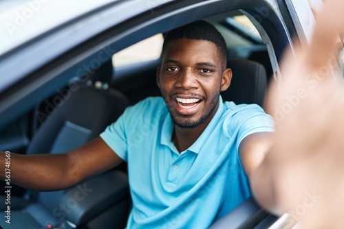 Young african american man making selfie by the camera sitting on car at street © Krakenimages.com
