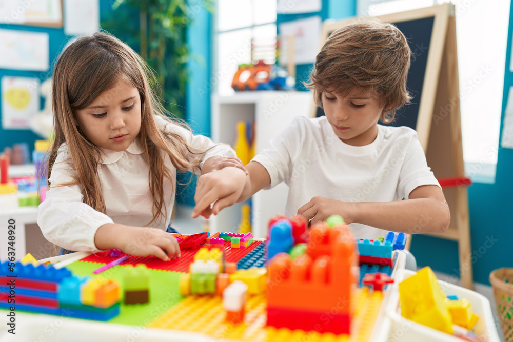 Fototapeta premium Brother and sister playing with construction blocks sitting on table at kindergarten