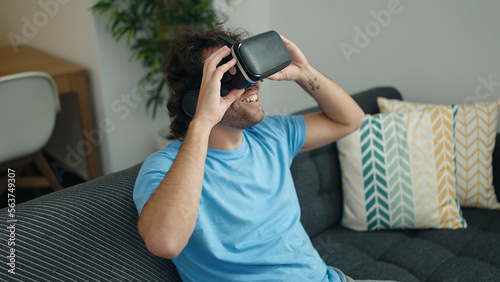 Young hispanic man playing video game using virtual reality glasses at home