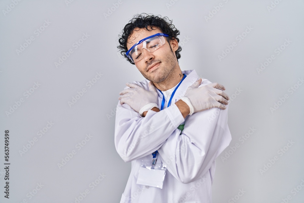 Hispanic man working at scientist laboratory hugging oneself happy and positive, smiling confident. self love and self care Hispanic man working at scientist laboratory hugging oneself happy and positive, smiling confident. self love and self care