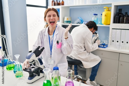 Young two people working at scientist laboratory celebrating victory with happy smile and winner expression with raised hands