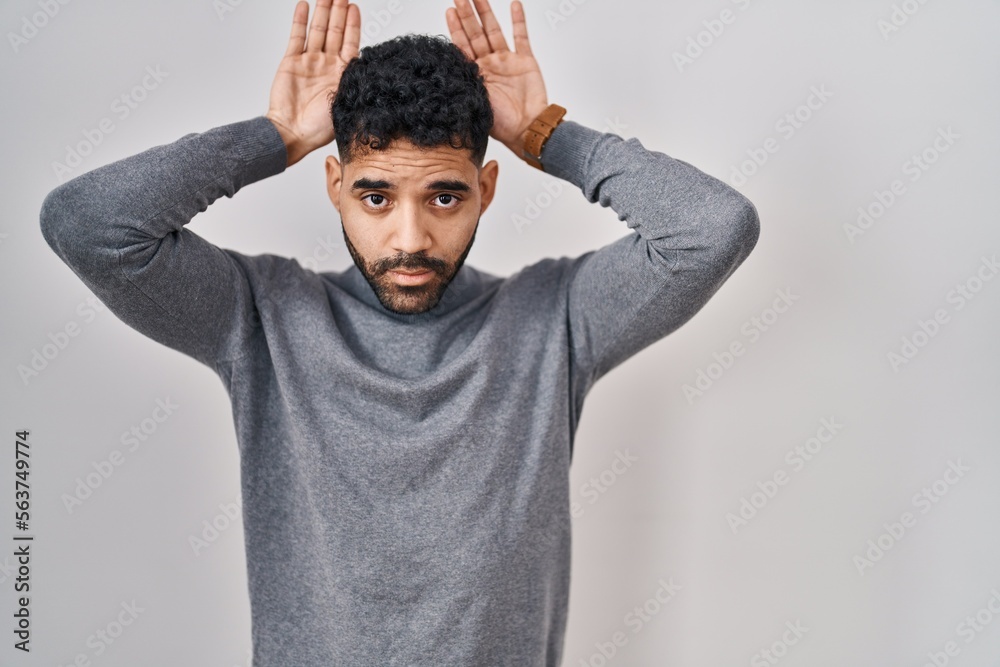 Hispanic man with beard standing over white background doing bunny ears gesture with hands palms looking cynical and skeptical. easter rabbit concept. Hispanic man with beard standing over white background doing bunny ears gesture with hands palms looking cynical and skeptical. easter rabbit concept.
