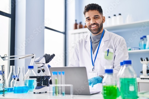 Young hispanic man wearing scientist uniform using laptop at laboratory