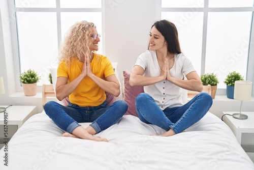 Two women mother and daughter doing yoga exercise sitting on bed at bedroom