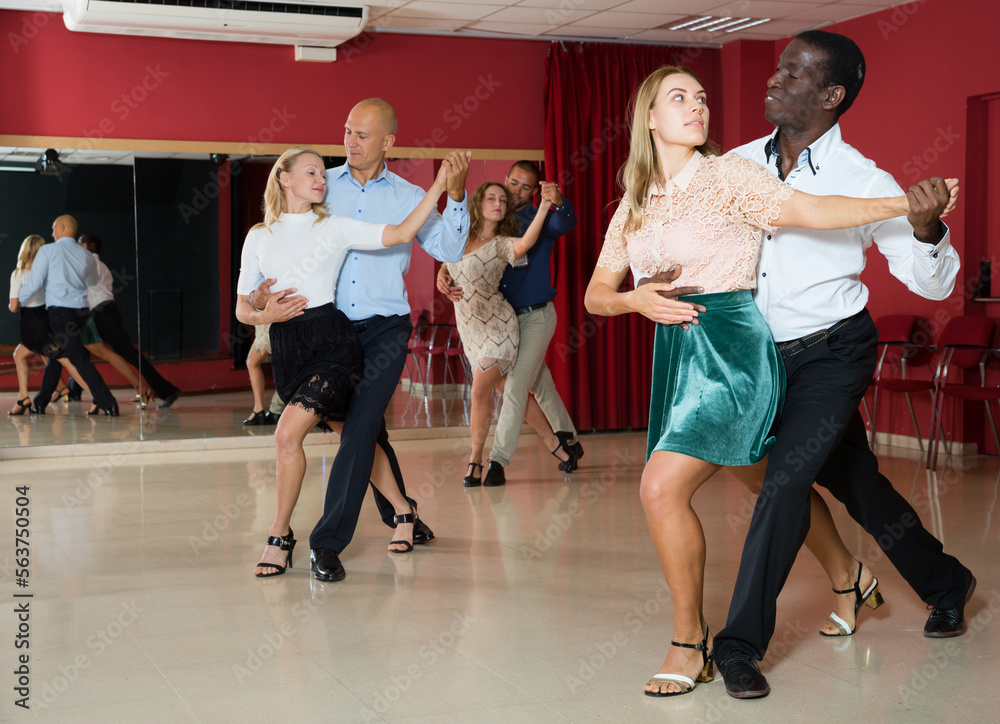Adult dancing couples enjoying latin dances in modern studio..
