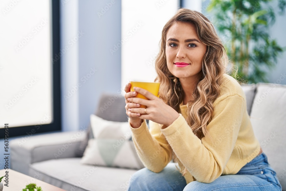 Young woman drinking coffee sitting on sofa at home Young woman drinking coffee sitting on sofa at home