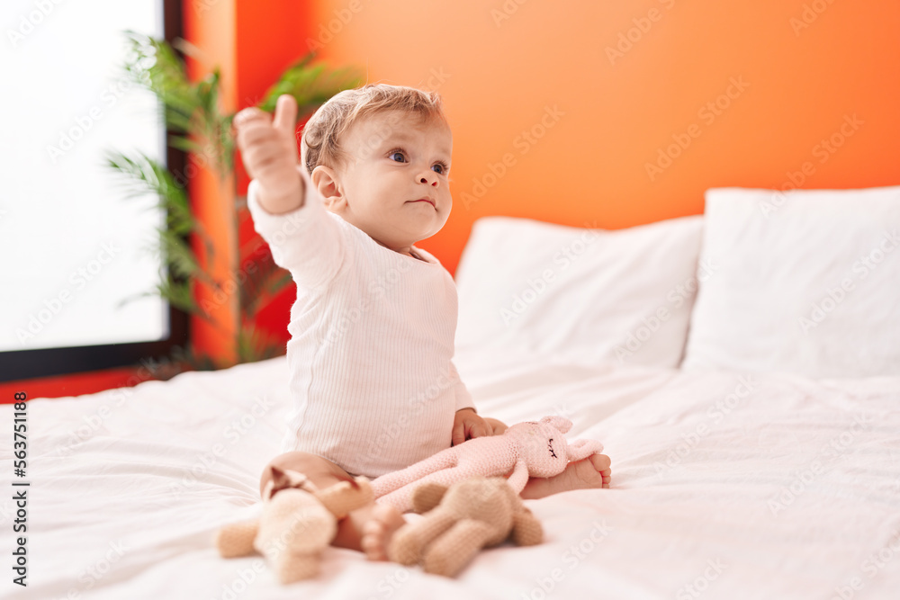 Adorable blond toddler holding doll sitting on bed at bedroom Adorable blond toddler holding doll sitting on bed at bedroom