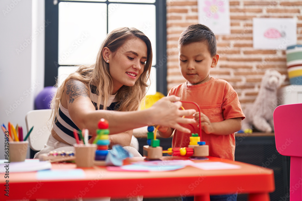 Teacher and toddler playing with toys sitting on table at kindergarten Teacher and toddler playing with toys sitting on table at kindergarten
