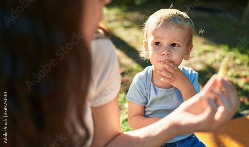 Mother and son sitting on bench together eating little worms snack at park