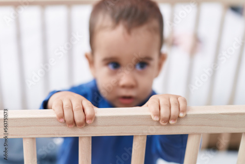 Adorable hispanic toddler standing on cradle at bedroom