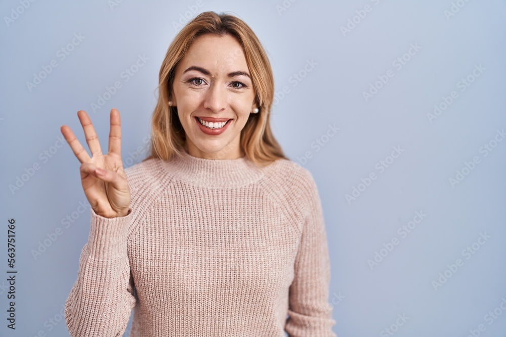 Hispanic woman standing over blue background showing and pointing up with fingers number three while smiling confident and happy. Hispanic woman standing over blue background showing and pointing up with fingers number three while smiling confident and happy.