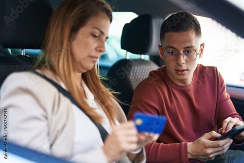 Man and woman mother and son using smartphone and credit card sitting on car at street