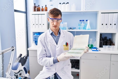 Caucasian man working at scientist laboratory in shock face  looking skeptical and sarcastic  surprised with open mouth