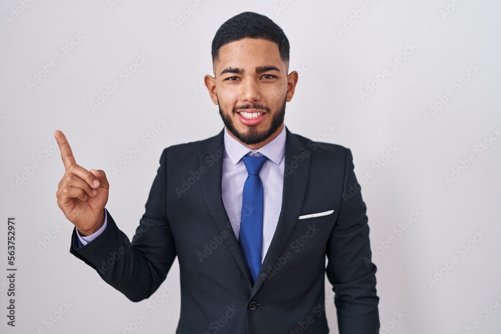 Young hispanic man wearing business suit and tie with a big smile on face, pointing with hand finger to the side looking at the camera. Young hispanic man wearing business suit and tie with a big smile on face, pointing with hand finger to the side looking at the camera.