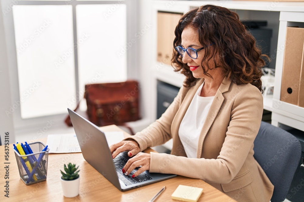 Middle age hispanic woman smiling working with laptop at the office
