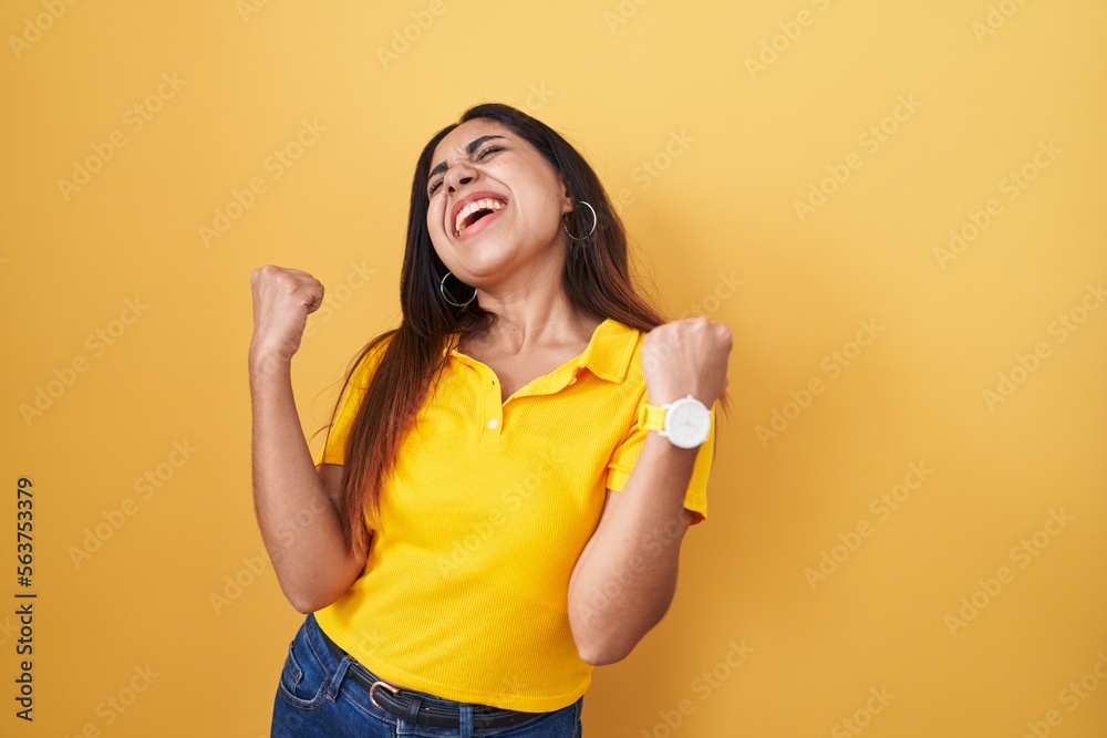 Young arab woman standing over yellow background celebrating surprised and amazed for success with arms raised and eyes closed. winner concept. Young arab woman standing over yellow background celebrating surprised and amazed for success with arms raised and eyes closed. winner concept.