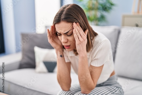 Young beautiful hispanic woman suffering for headache sitting on sofa at home