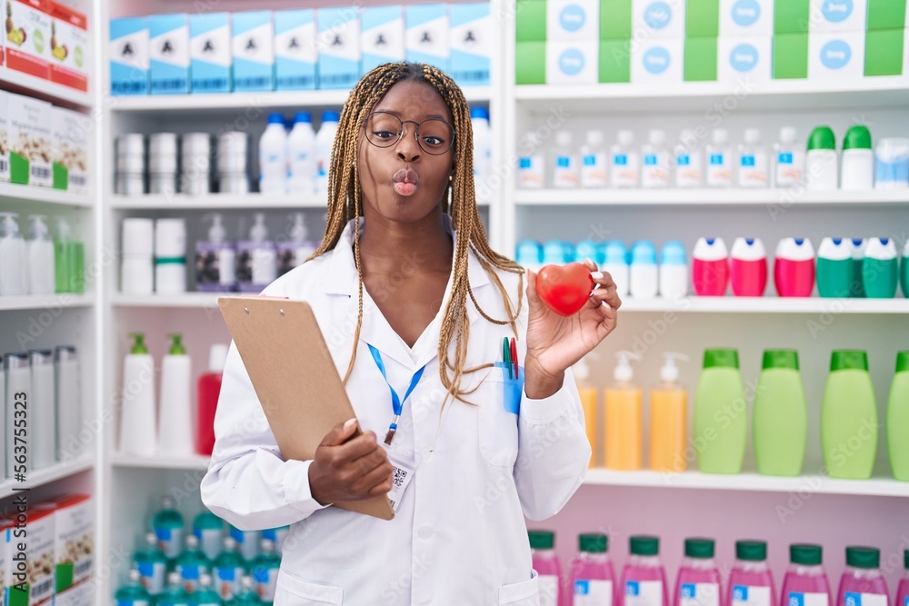African american woman with braided hair working at pharmacy drugstore making fish face with mouth and squinting eyes, crazy and comical. African american woman with braided hair working at pharmacy drugstore making fish face with mouth and squinting eyes, crazy and comical.