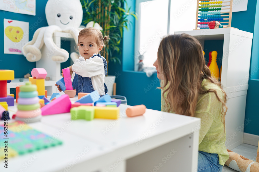 Fototapeta premium Teacher and toddler playing with geometry blocks sitting on table at kindergarten