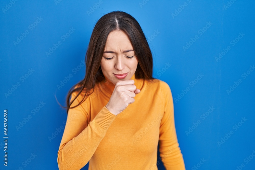 Fototapeta premium Young brunette woman standing over blue background feeling unwell and coughing as symptom for cold or bronchitis. health care concept.
