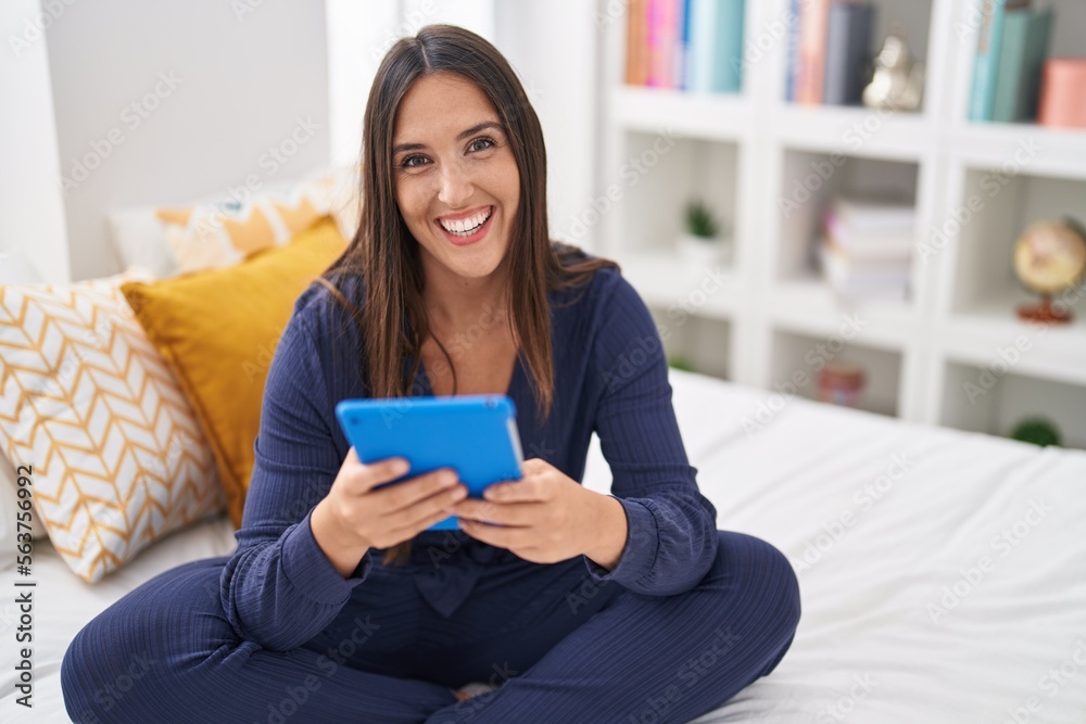 Young beautiful hispanic woman using touchpad sitting on bed at bedroom Young beautiful hispanic woman using touchpad sitting on bed at bedroom