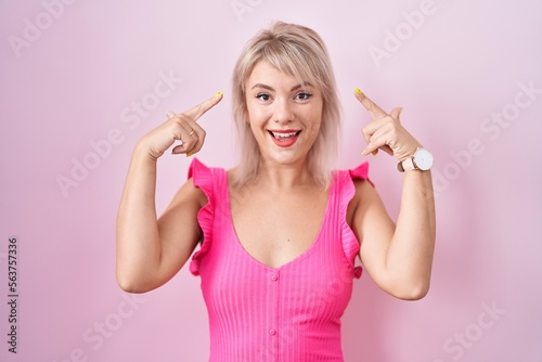 Young caucasian woman standing over pink background smiling pointing to head with both hands finger, great idea or thought, good memory © Krakenimages.com