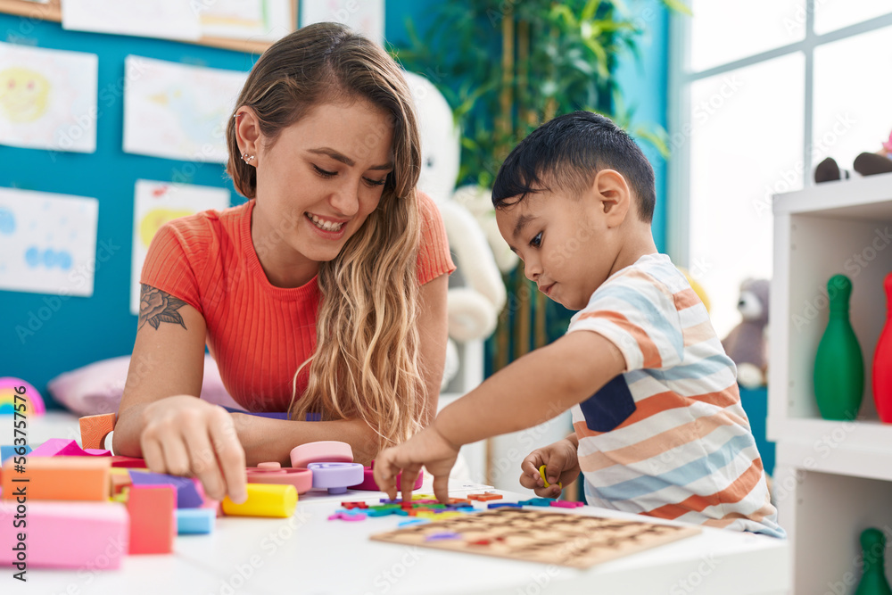 Teacher and toddler playing with maths puzzle game sitting on table at kindergarten Teacher and toddler playing with maths puzzle game sitting on table at kindergarten