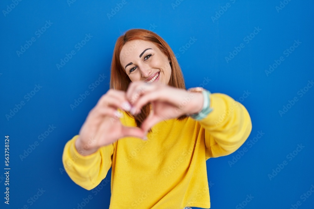 Young woman standing over blue background smiling in love doing heart symbol shape with hands. romantic concept. Young woman standing over blue background smiling in love doing heart symbol shape with hands. romantic concept.