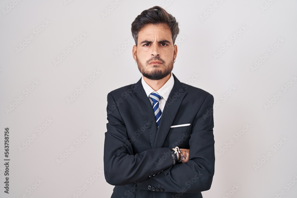 Young hispanic man with tattoos wearing business suit and tie skeptic and nervous, disapproving expression on face with crossed arms. negative person. Young hispanic man with tattoos wearing business suit and tie skeptic and nervous, disapproving expression on face with crossed arms. negative person.