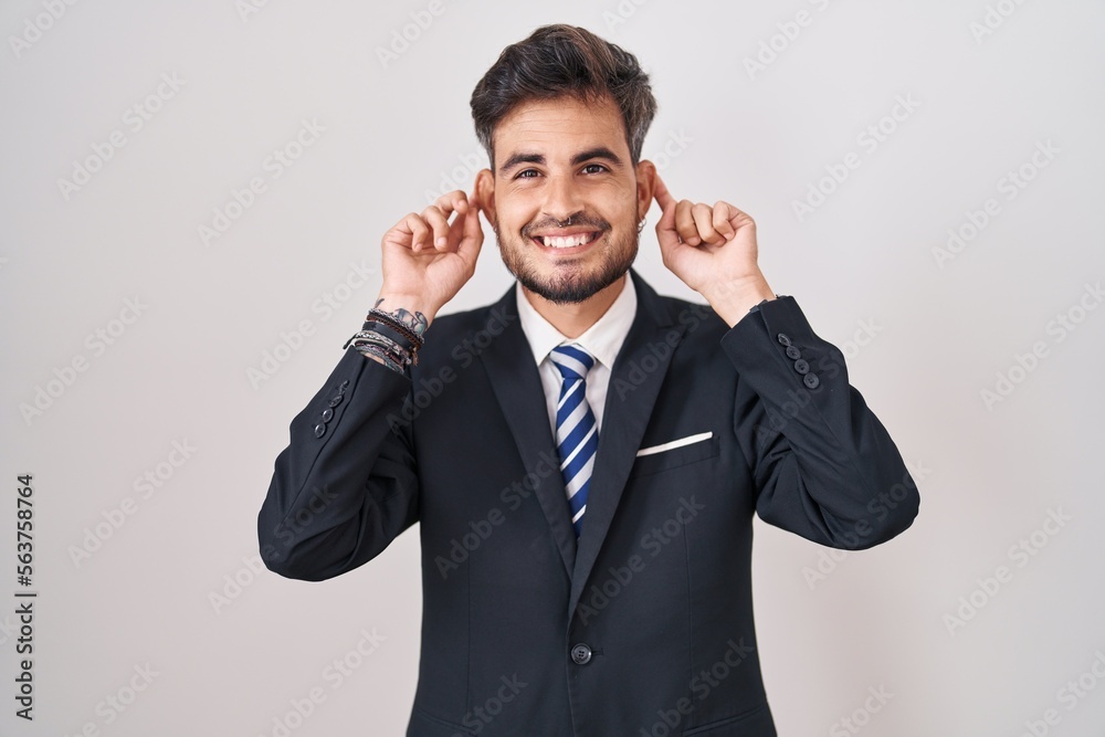 Young hispanic man with tattoos wearing business suit and tie smiling pulling ears with fingers, funny gesture. audition problem Young hispanic man with tattoos wearing business suit and tie smiling pulling ears with fingers, funny gesture. audition problem