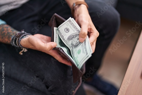 Young hispanic man holding dollars on wallet sitting on sofa at home