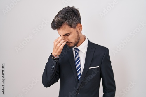 Young hispanic man with tattoos wearing business suit and tie tired rubbing nose and eyes feeling fatigue and headache. stress and frustration concept.