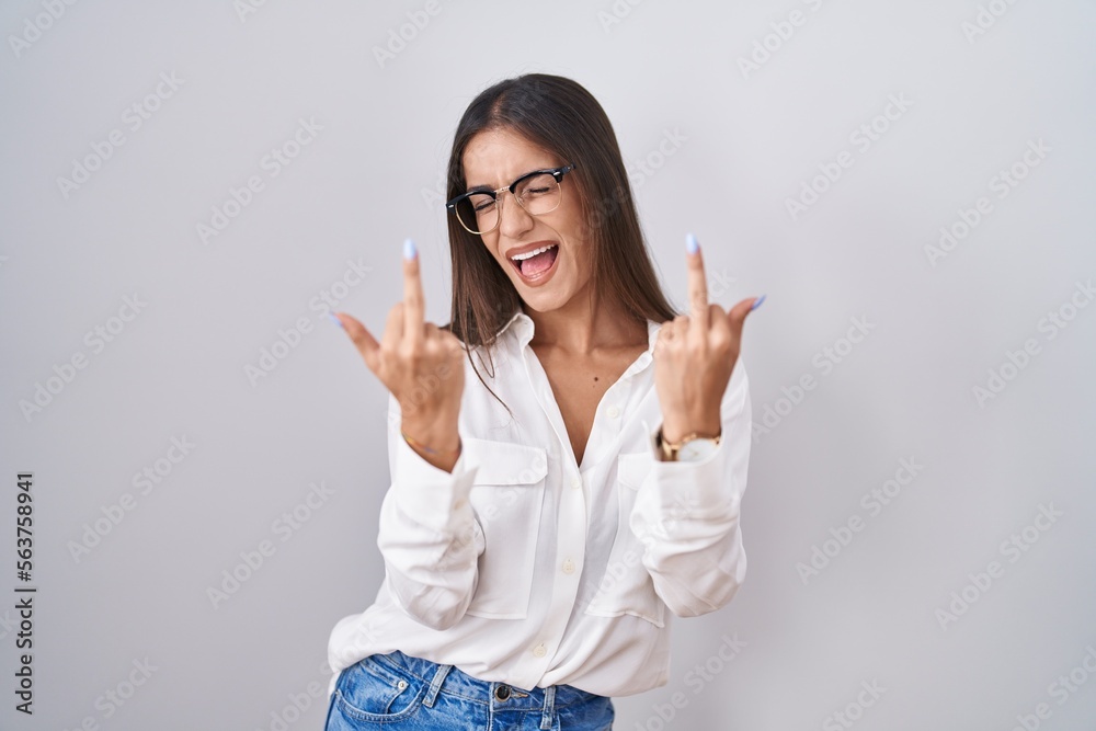 Young brunette woman wearing glasses showing middle finger doing fuck you bad expression, provocation and rude attitude. screaming excited