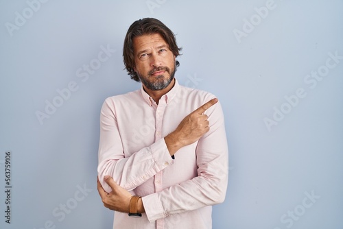 Handsome middle age man wearing elegant shirt background pointing with hand finger to the side showing advertisement, serious and calm face