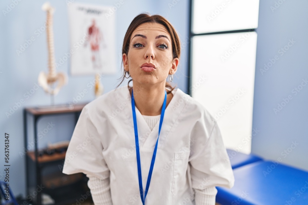 Young brunette woman working at pain recovery clinic looking at the camera blowing a kiss on air being lovely and sexy. love expression.