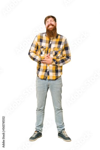 Young adult redhead man with a long beard standing full body isolated touches tummy, smiles gently, eating and satisfaction concept.