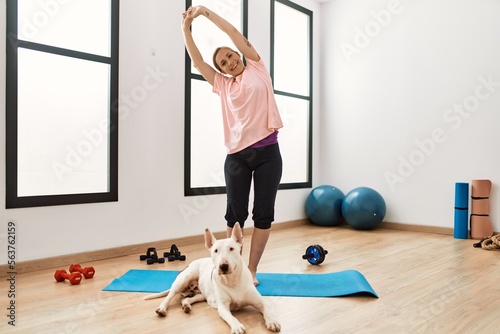 Young caucasian woman smiling confident stretching with dog at sport center