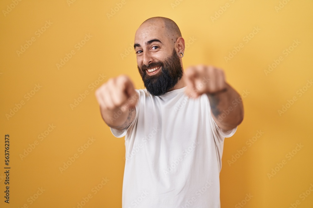 Young hispanic man with beard and tattoos standing over yellow background pointing to you and the camera with fingers, smiling positive and cheerful Young hispanic man with beard and tattoos standing over yellow background pointing to you and the camera with fingers, smiling positive and cheerful