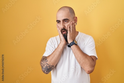 Young hispanic man with beard and tattoos standing over yellow background tired hands covering face  depression and sadness  upset and irritated for problem