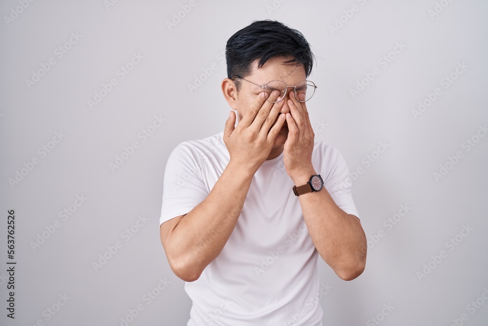Young asian man standing over white background rubbing eyes for fatigue and headache, sleepy and tired expression. vision problem Young asian man standing over white background rubbing eyes for fatigue and headache, sleepy and tired expression. vision problem