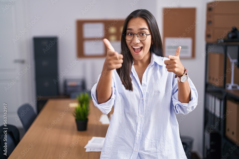 Young hispanic woman at the office pointing fingers to camera with happy and funny face. good energy and vibes. Young hispanic woman at the office pointing fingers to camera with happy and funny face. good energy and vibes.
