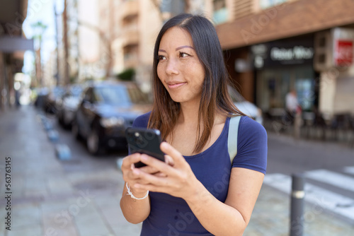 Young asian woman smiling confident using smartphone at street
