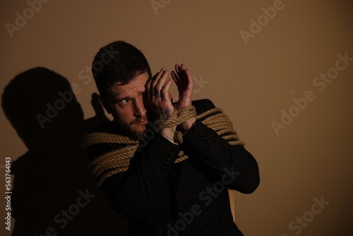 Scared man tied up and taken hostage on dark background. Space for text