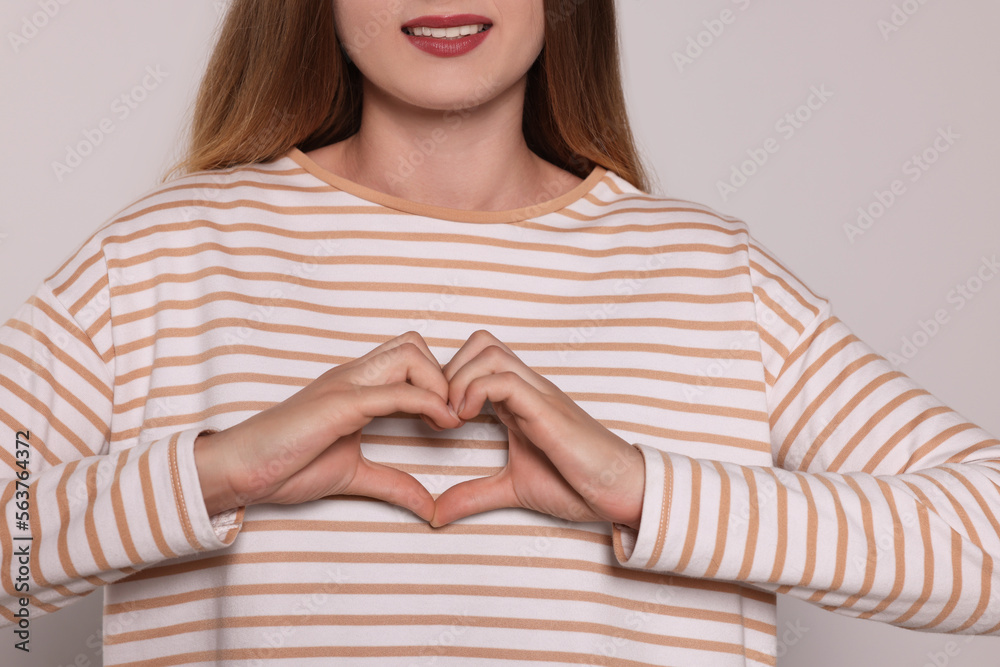Young woman making heart with hands on light grey background, closeup. Volunteer concept Young woman making heart with hands on light grey background, closeup. Volunteer concept