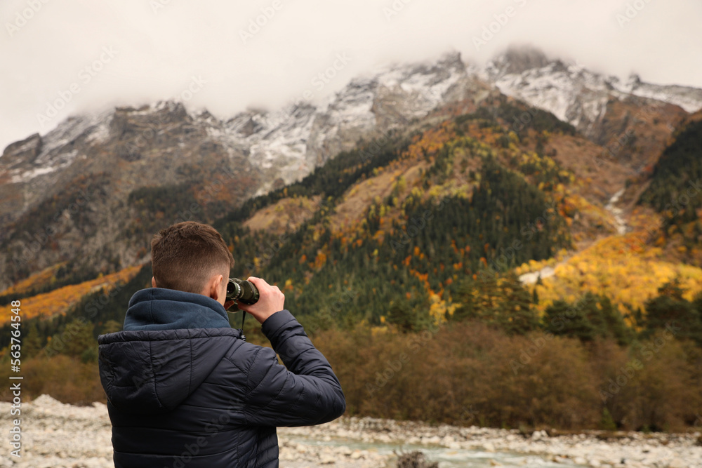 Boy looking through binoculars in beautiful mountains, back view. Space for text