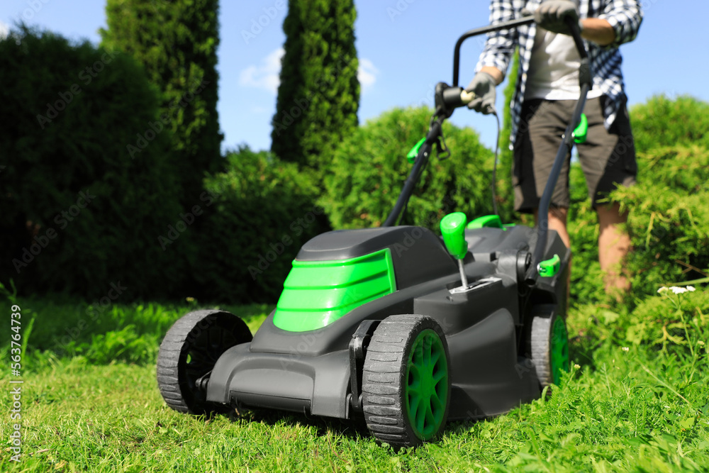 Fototapeta premium Man turning on lawn mower in garden, closeup. Cutting grass