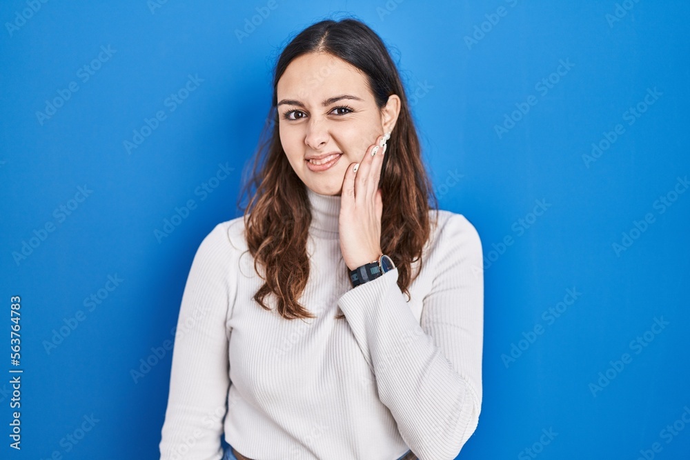 Young hispanic woman standing over blue background touching mouth with hand with painful expression because of toothache or dental illness on teeth. dentist Young hispanic woman standing over blue background touching mouth with hand with painful expression because of toothache or dental illness on teeth. dentist